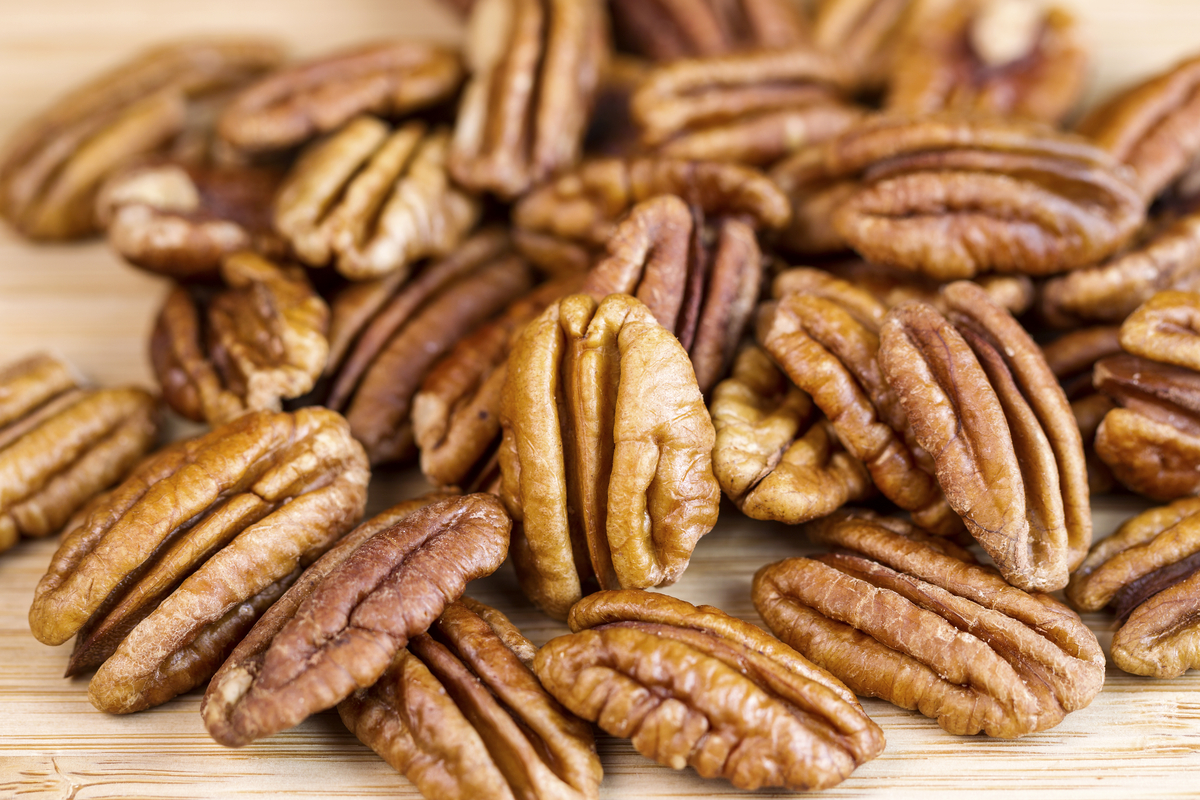 Horizontal photo of slightly roasted pecan nuts with focus of standing pecan in front of pile on natural wood