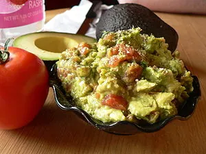 A bowl of guacamole beside a tomato and a cut ... A bowl of guacamole beside a tomato and a cut ...