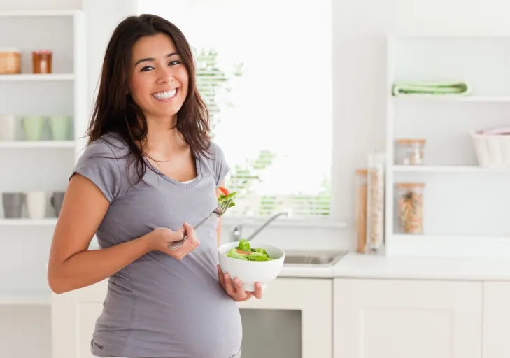 Attractive pregnant woman holding a bowl of salad while standing