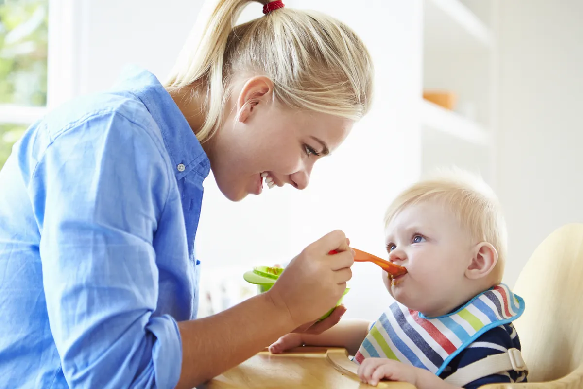 Mother Feeding Baby Boy In High Chair
