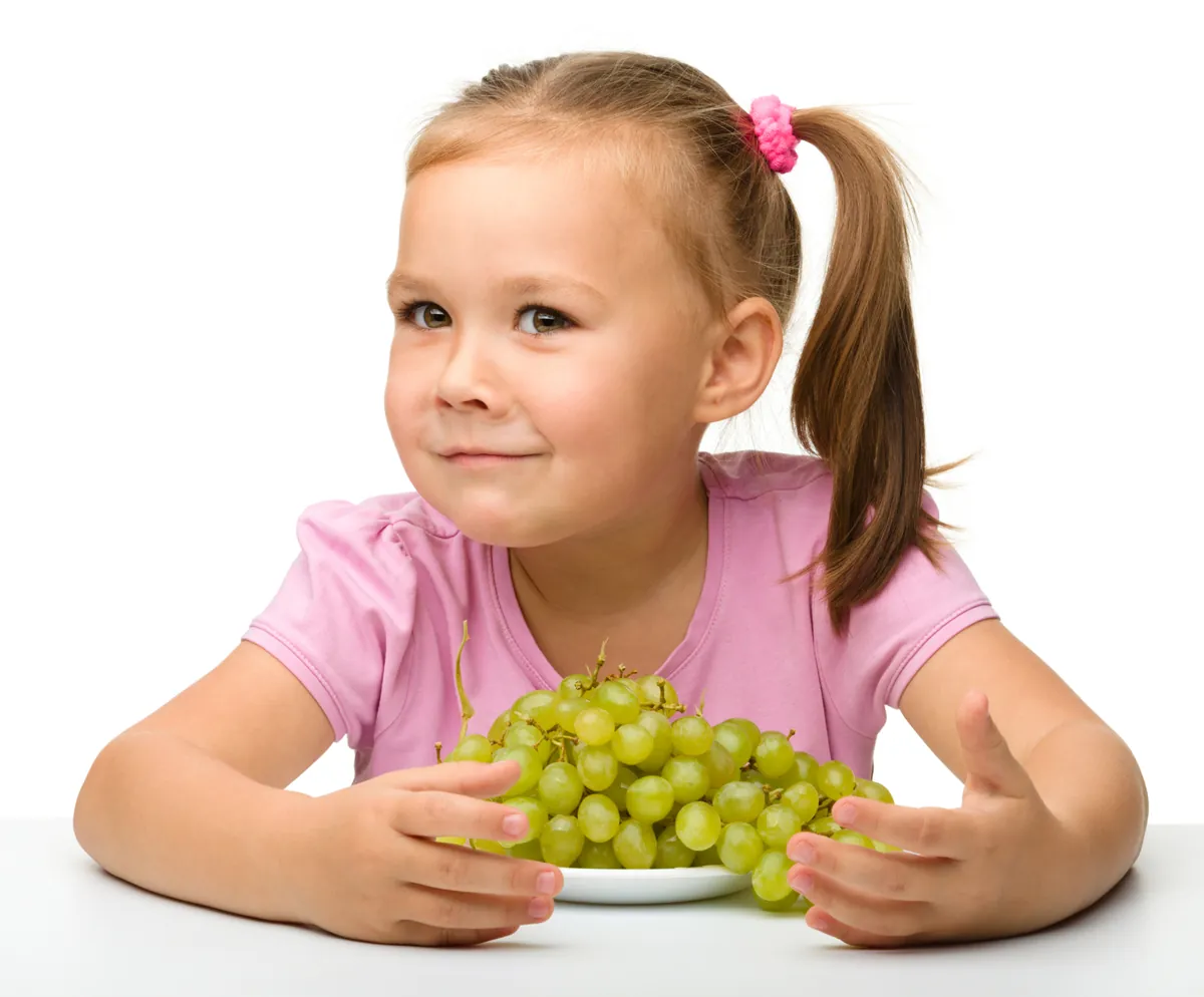 Little girl is eating grapes, isolated over white