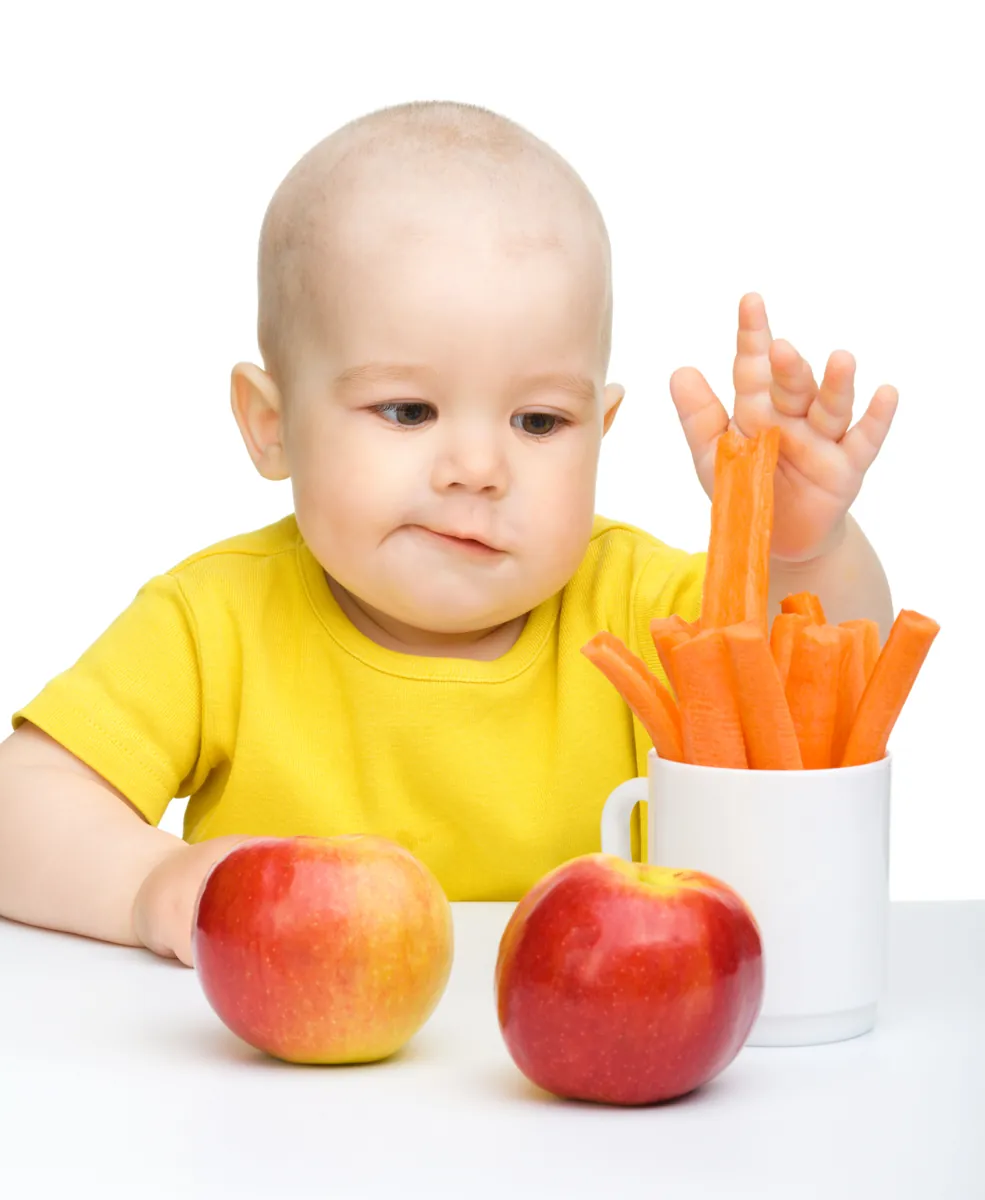 Little boy pulling up carrot from a cup, isolated over white