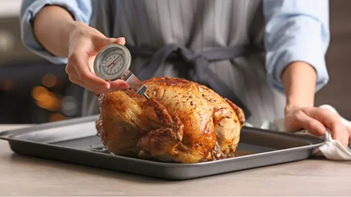 Male checking the temperature of a chicken sitting on a baking sheet