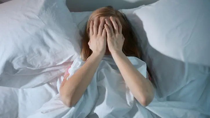 Woman laying awake in bed with her hands over her face