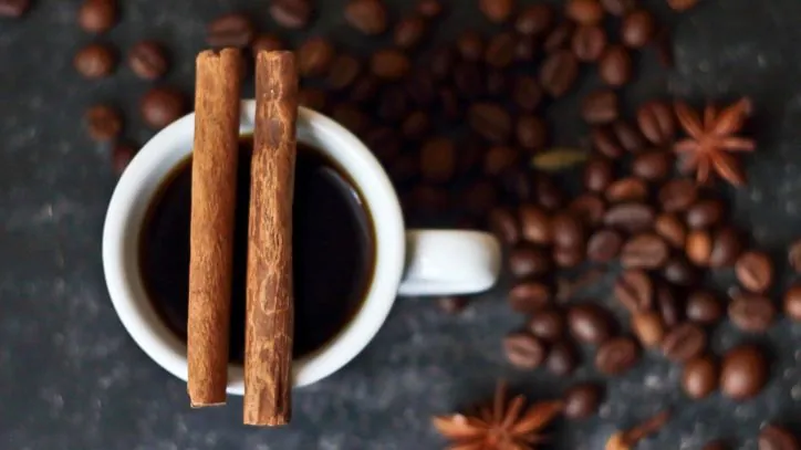 Two cinnamon sticks sitting across the top of a mug filled with coffee