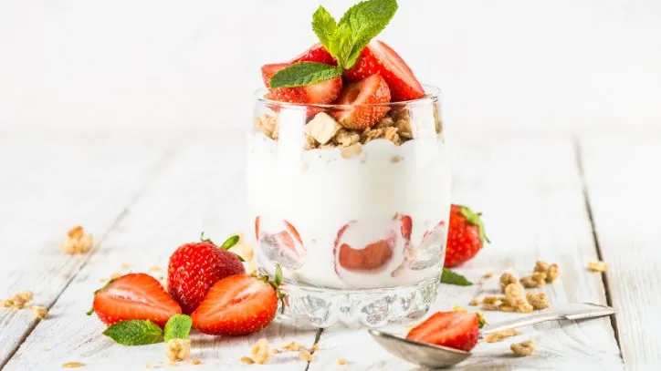 Glass filled with greek yogurt, granola and strawberries