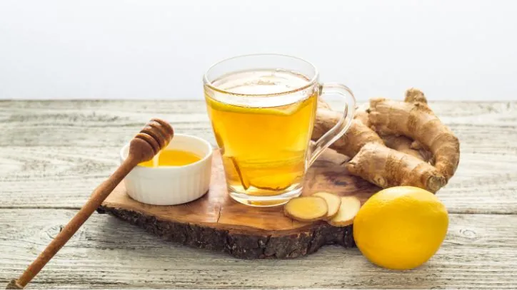 Hot cup of tea with honey and ginger next to it