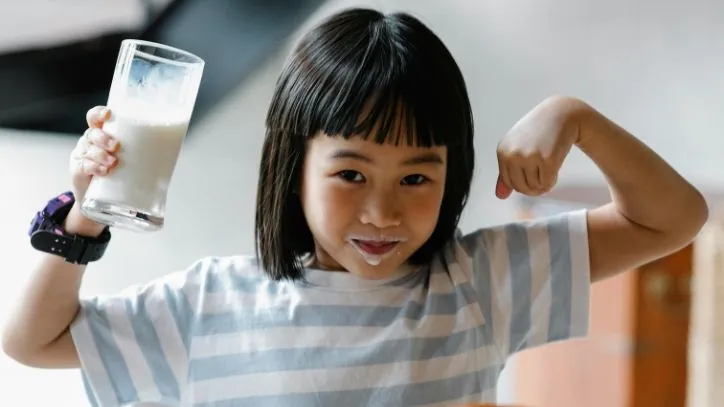 Little girl drinking milk while lifting up her arms to show her muscles