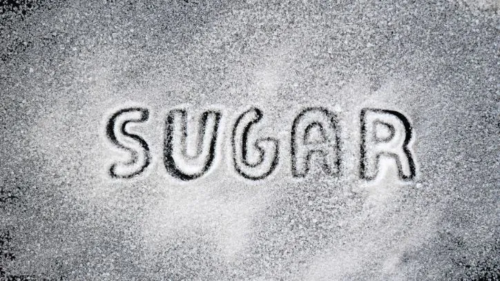 The word "sugar" written in spilled sugar on a table