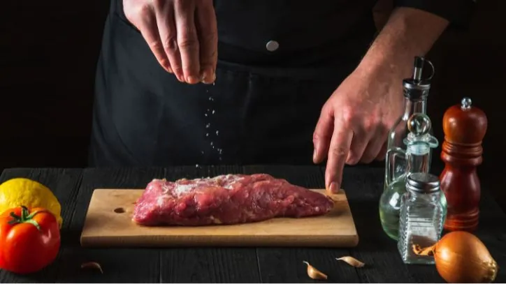 man seasoning red meat with salt