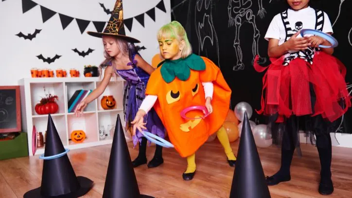 Three young girls dressed in Halloween costumes playing a Halloween ring toss game