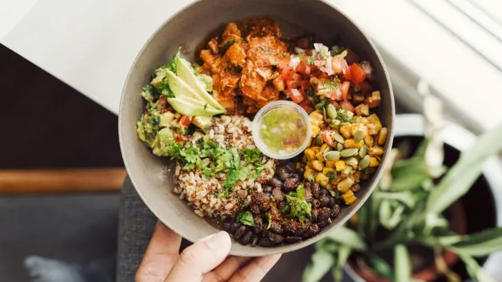 hand holding a harvest bowl filled with local seasonal produce