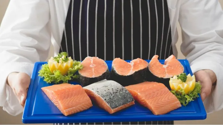 Various cuts of fish sitting on a cutting board that is being held by a chef