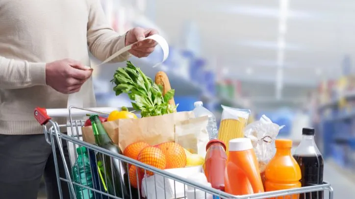 man looking at a grocery reciept over a cart of groceries