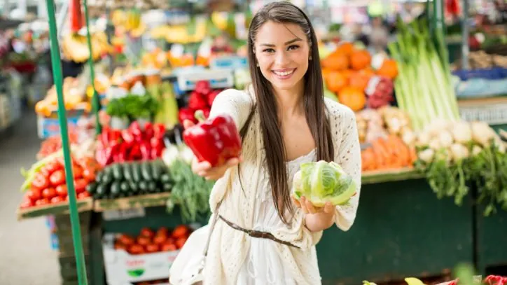 Woman holding upa red bell pepper while shopping at a Farmers' Market