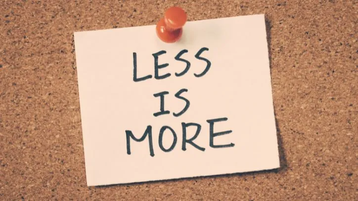 Post-it note pinned to a cork board that reads "Less is more"