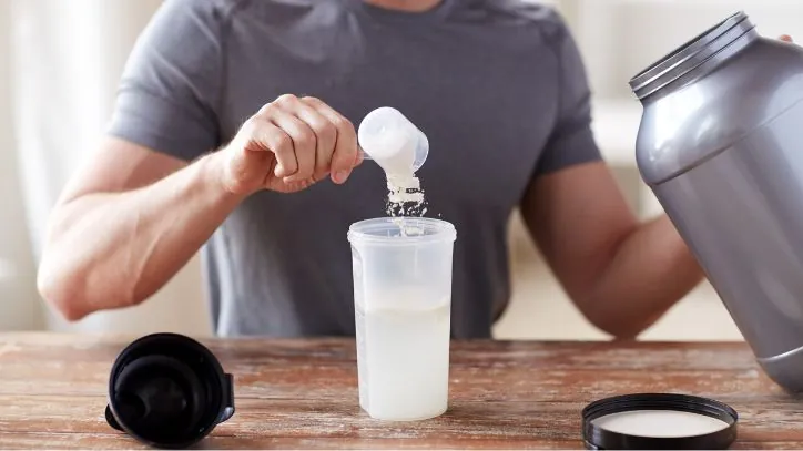 a male dumping a scoop of protein powder into a shaker cup