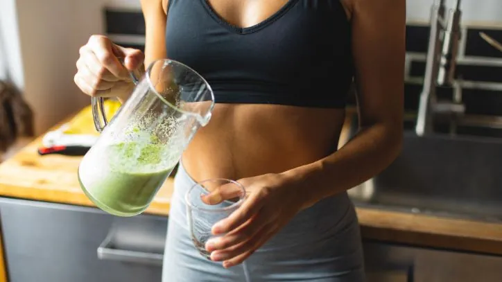 woman pouring green smoothie into a glass